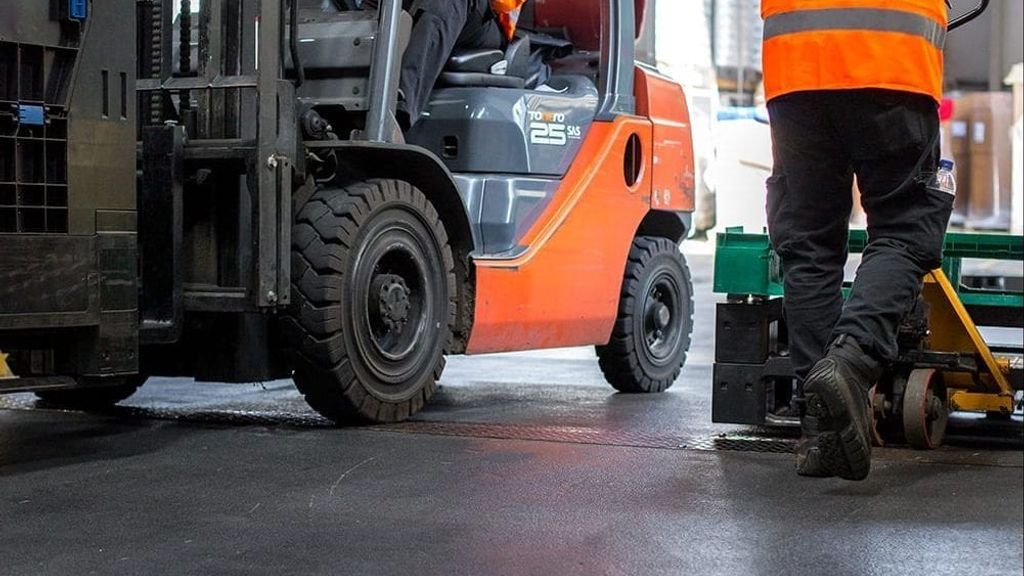 A forklift truck being manner with a worker next to it pushing a pallet
